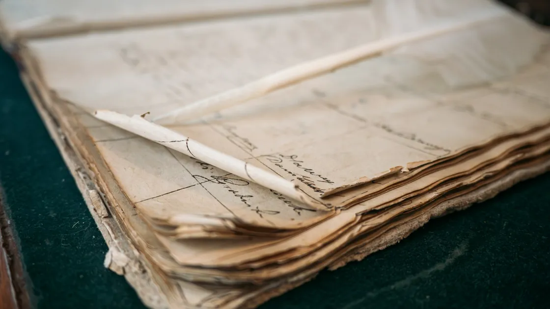 Legajo de documentos manuscritos con los bordes oscurecidos y ondulados sobre una mesa de trabajo